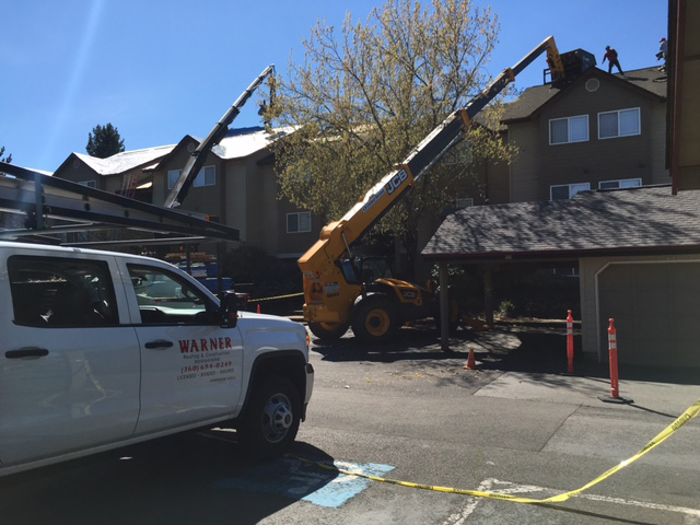Warner Construction truck in foreground as a crane lifts roofing materials to the top of a home.