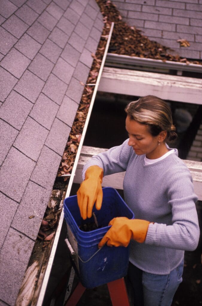 woman cleaning out gutters on roof