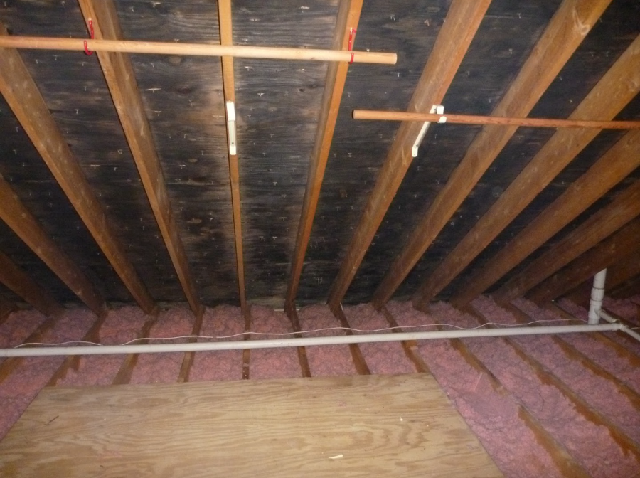 Image of an attic with pink insulation along the joists to help illustrate Roof Structure Repair.