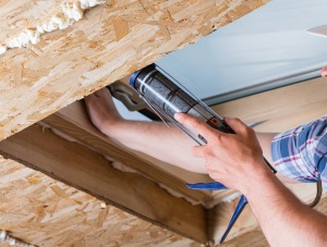 Someone applying sealant to the interior of a skylight to help illustrate installing a skylight, Vancouver Skylight Repair Warner Roofing, Do I Need a Permit to Install a Skylight, and How to Install Skylights on a Low-Slope Roof.
