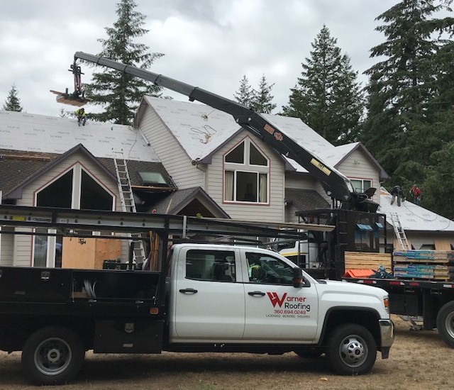 Roof installation using a crane and Warner Roofing truck out front with a flatbed full of shingles to help illustrate residential roofing types.