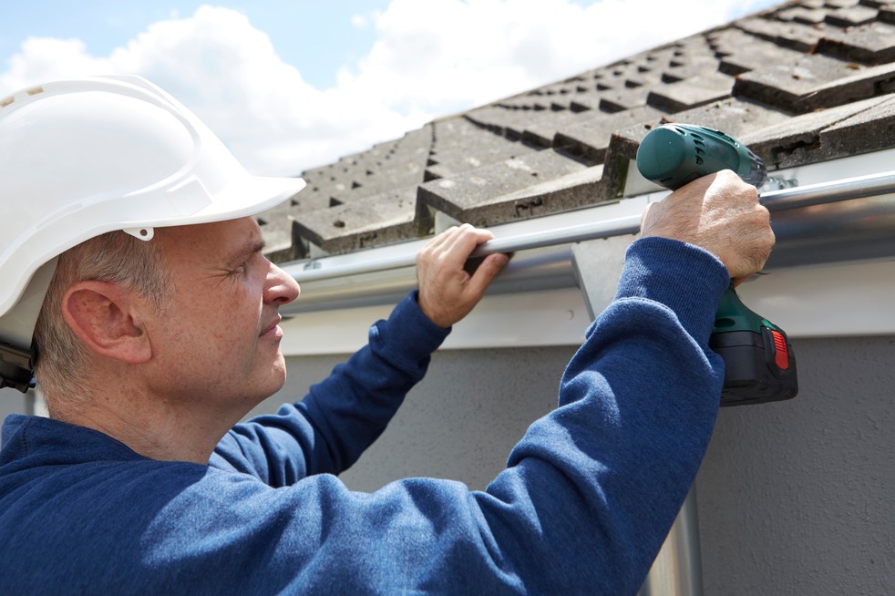 Workman Repairing Guttering On Exterior Of House