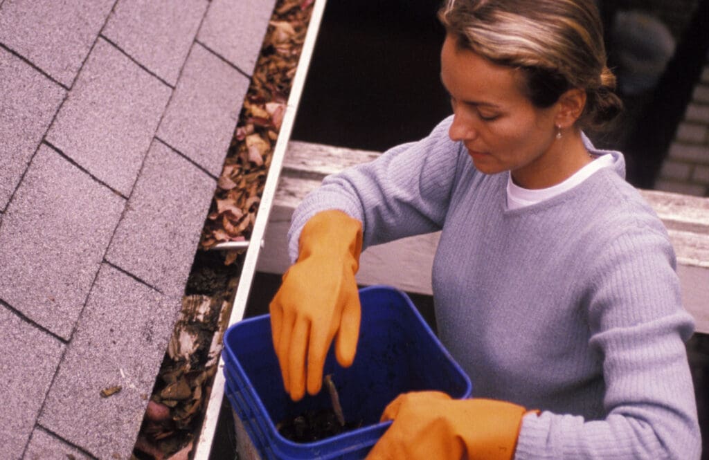 Woman cleaning leaves out of a gutter
