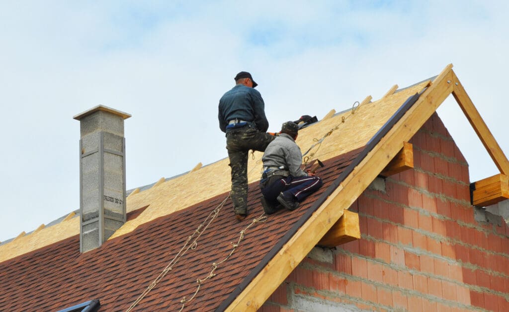 Two workers installing a roof on a brick building