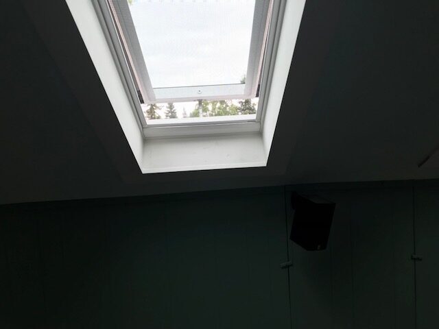 Interior view looking up at a freshly installed, open solar-powered venting skylight letting natural light and fresh air into a residential home.