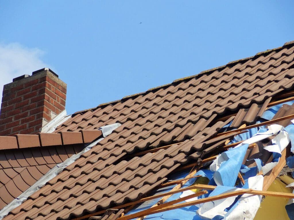 Home with roof being replaced showing new shingles, felt paper, and tools. Blue sky in background.