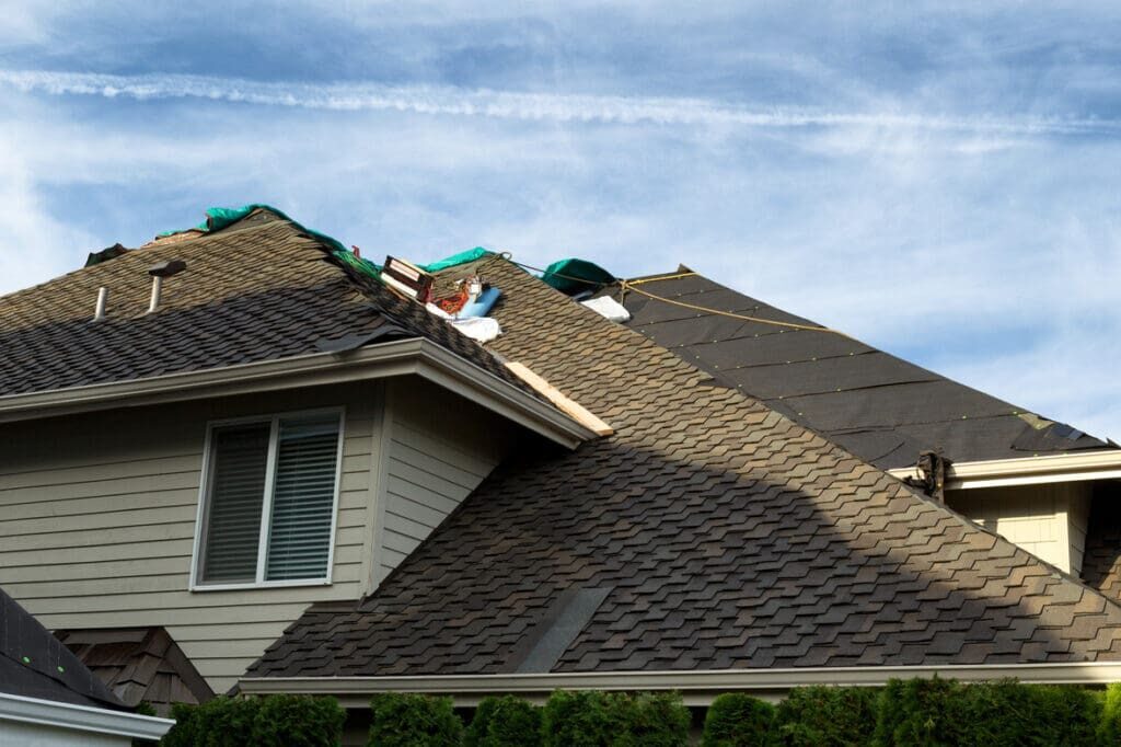 Home with roof being replaced showing new shingles, felt paper, and tools. Blue sky in background.