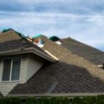 Home with roof being replaced showing new shingles, felt paper, and tools. Blue sky in background.