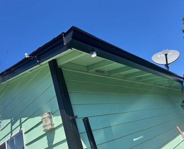 Image of a home with green siding and black gutter system to illustrate gutter installation