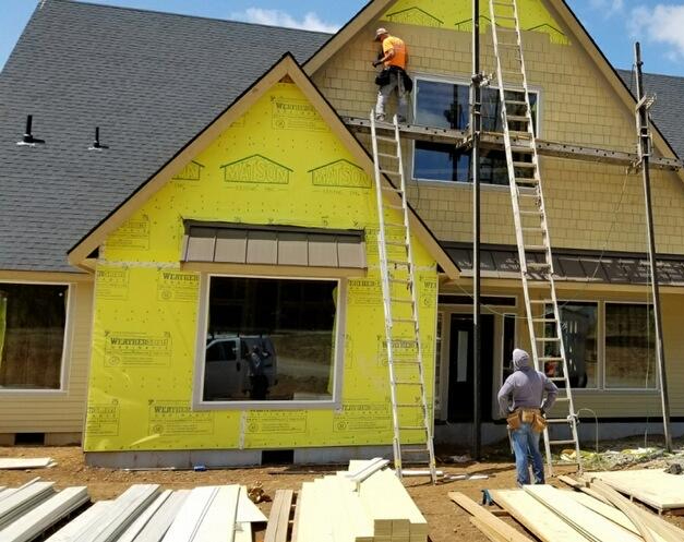 Two workers installing siding on a new home with new composite roofing to help illustrate what is synthetic composite roofing