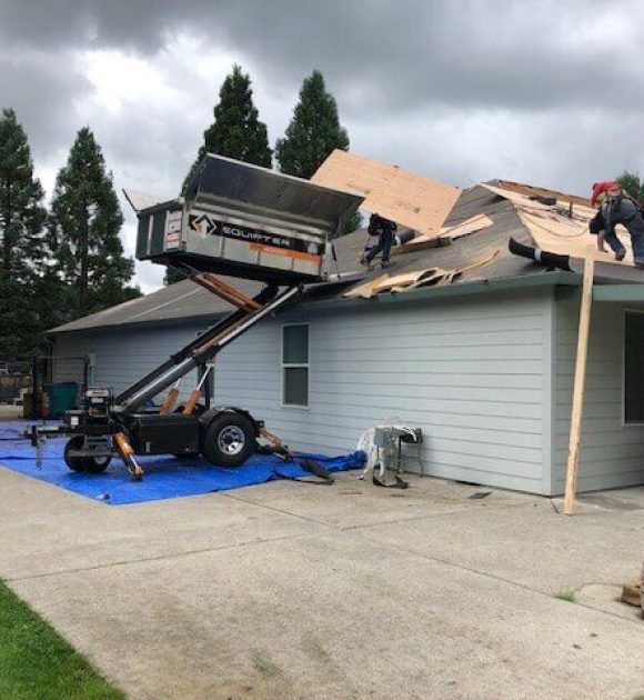 Roof tear off in process with a lifted dumpster to roof height to help illustrate roof replacements