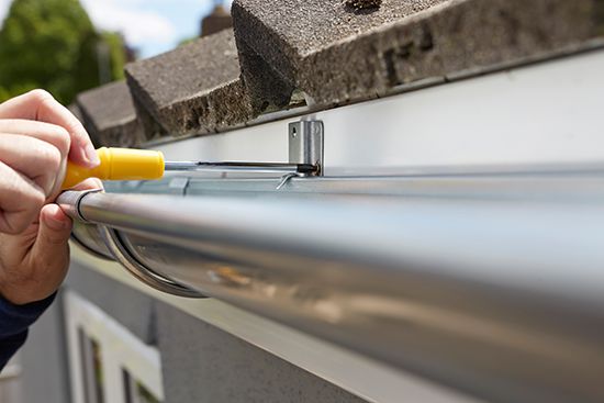 Close up of a gutter installation with a crew member adjusting the height of a gutter bracket