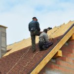 Two workers installing a roof on a brick building