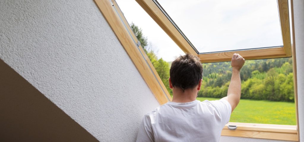 A man looking out an open skylight to illustrate Should I Replace Skylights When Reroofing and installing a skylight.